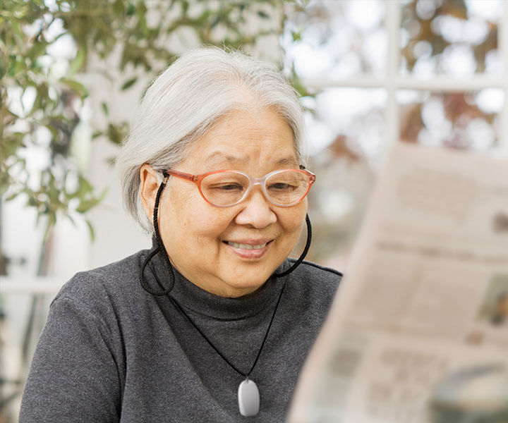 An elderly woman with glasses reading the newspaper.
