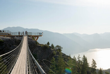 Cable bridge leading to a platform overlooking a lake surrounded by mountains