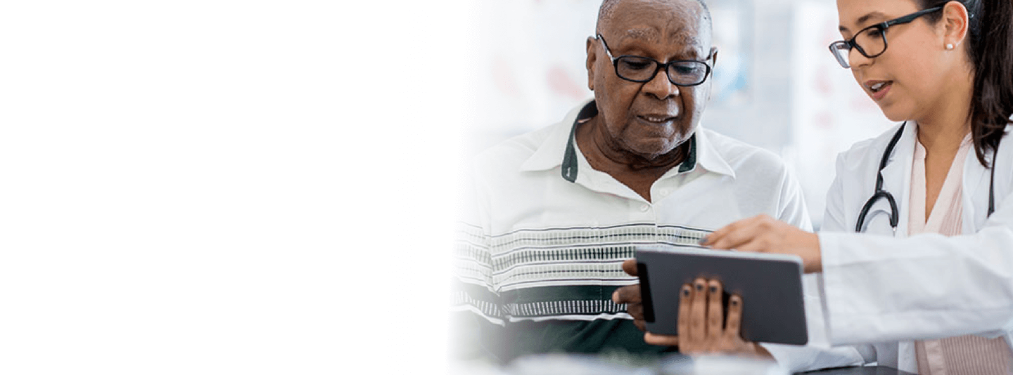 An elderly man sits with his young female doctor, reviewing his Electronic Medical Records on a tablet.