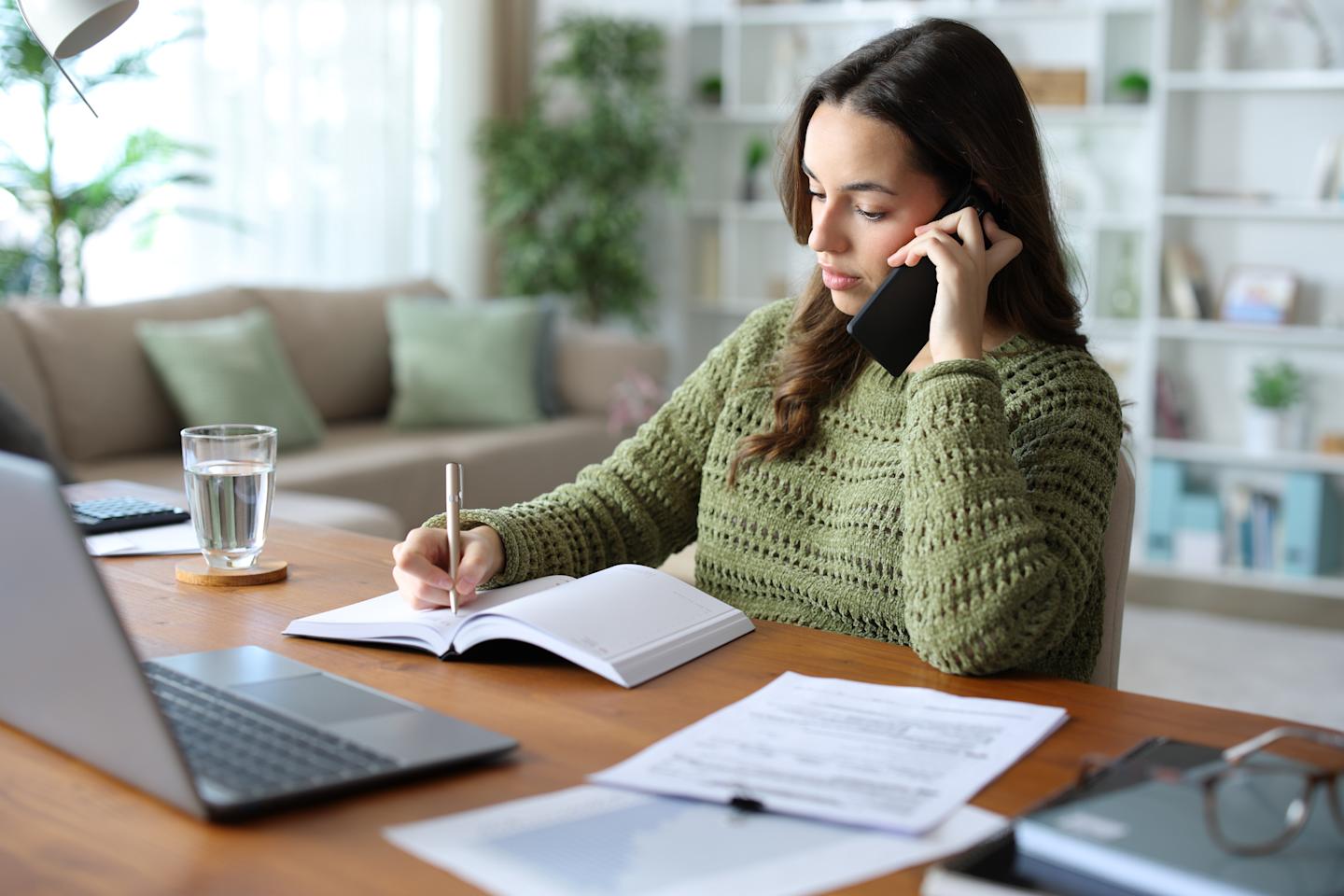 A person talking on the phone and taking notes.