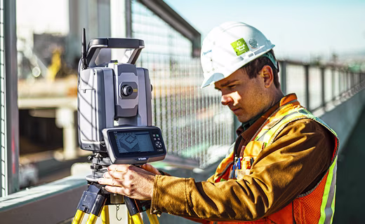Topógrafo en sitio de construcción junto a una cerca mira una estación total de Trimble.