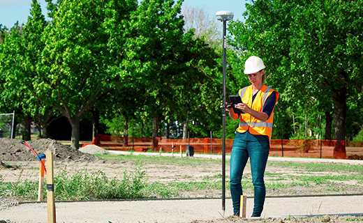 戴着安全帽的测绘人员站在住宅小区建筑工地,手持 Trimble GNSS 流动站系统进行测量。