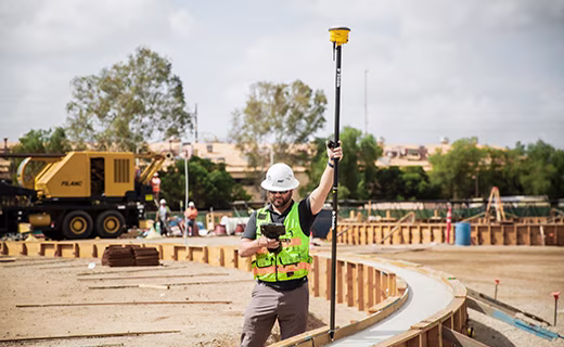 Construction worker on site holding a GNSS receiver pole reviewing data on a Trimble TSC7 data controller