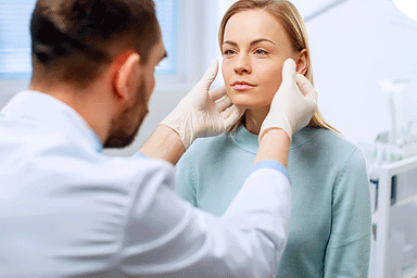 Plastic / Cosmetic Surgeon examines woman's face with gloved hands