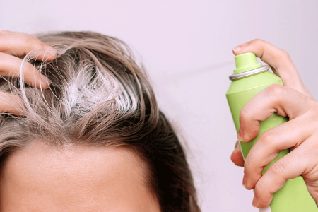 Close up of a woman spraying dry shampoo on the roots of her hair.