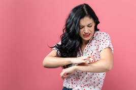 Young woman scratching her arm for itchy skin article from American Academy of Dermatology