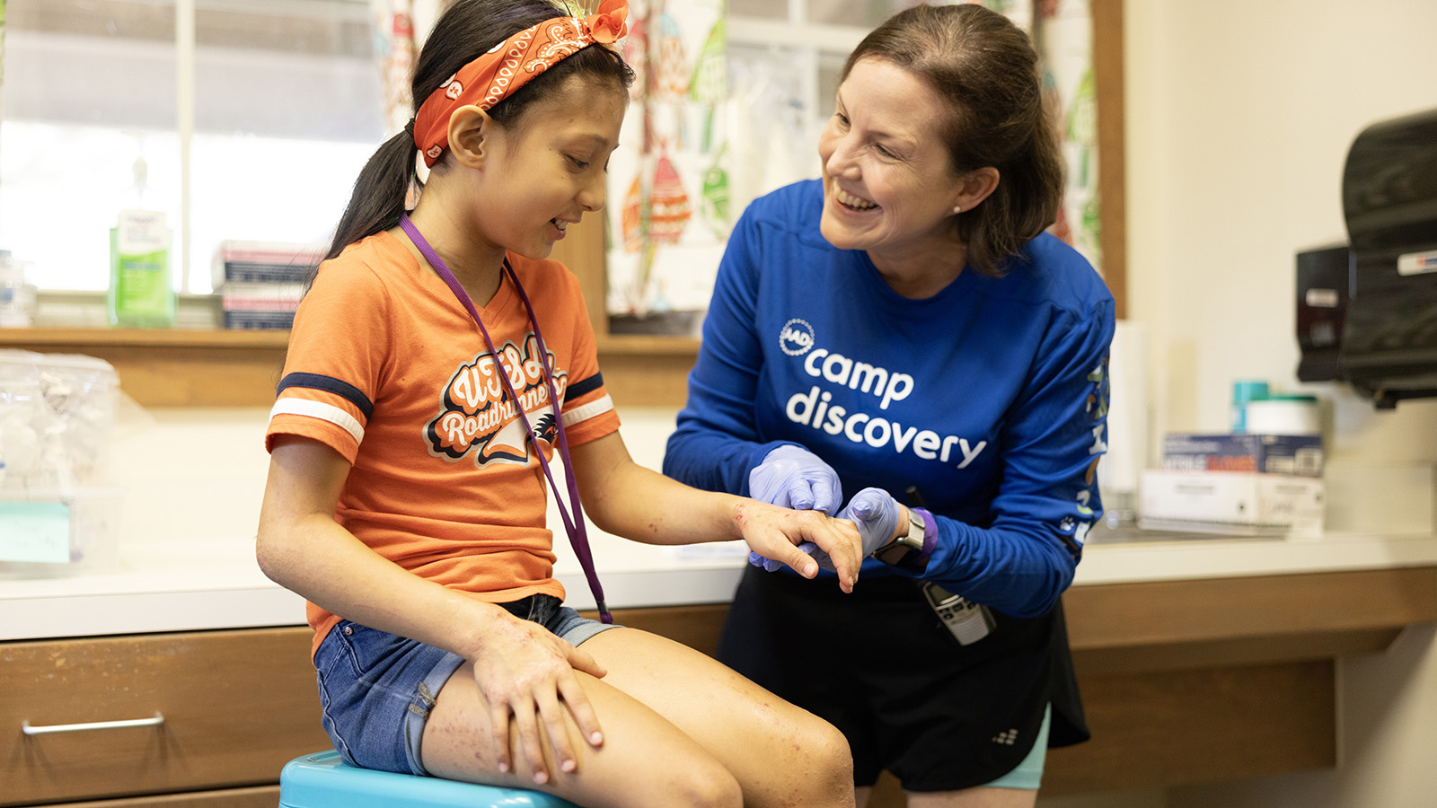 Young girl who is a camper at Camp Discovery pictured with a volunteer, an adult woman wearing a Camp Discovery shirt | American Academy of Dermatology (AAD).