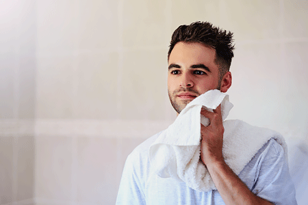 Young man drying his face with a towel in the bathroom