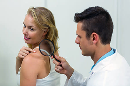 Woman pointing to a mole on her shoulder while getting a skin exam from her dermatologist