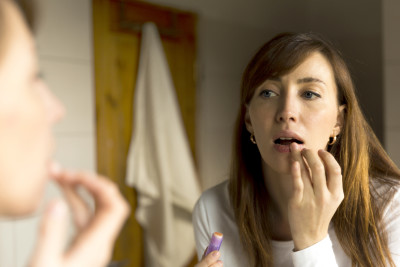 Woman applying lip balm in bathroom mirror