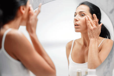  Woman applying face cream while looking in bathroom mirror
