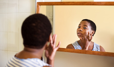 Woman looking in the mirror and applying moisturizer to her face