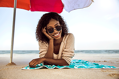 Young woman at the beach sitting under an umbrella.