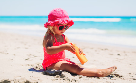 Young girl on the beach playing in sand wearing protection from the sun