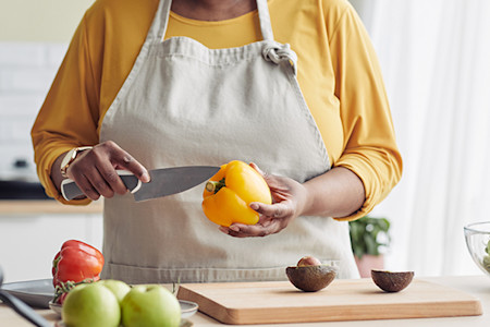 Woman preparing bell peppers and avocados with a knife at a kitchen counter