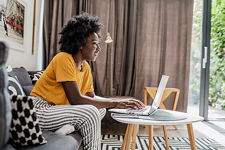 Woman sitting on couch at home, using laptop