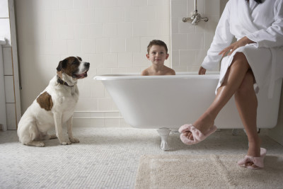Mother sitting on side of tub with son in bath tub and with dog