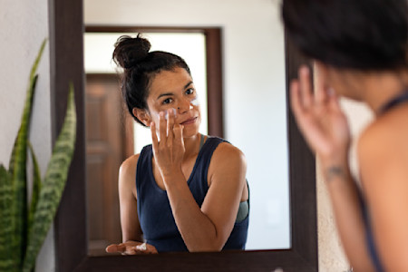 Woman applying sunscreen to help prevent early signs of aging like wrinkles and age spots.