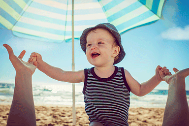 Baby with mother on the beach under an umbrella for sun protection