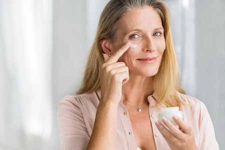 A woman in her 50s applying cream on her face