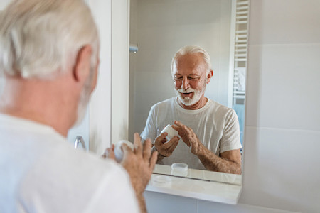 Senior man applying skincare cream in front of a bathroom mirror