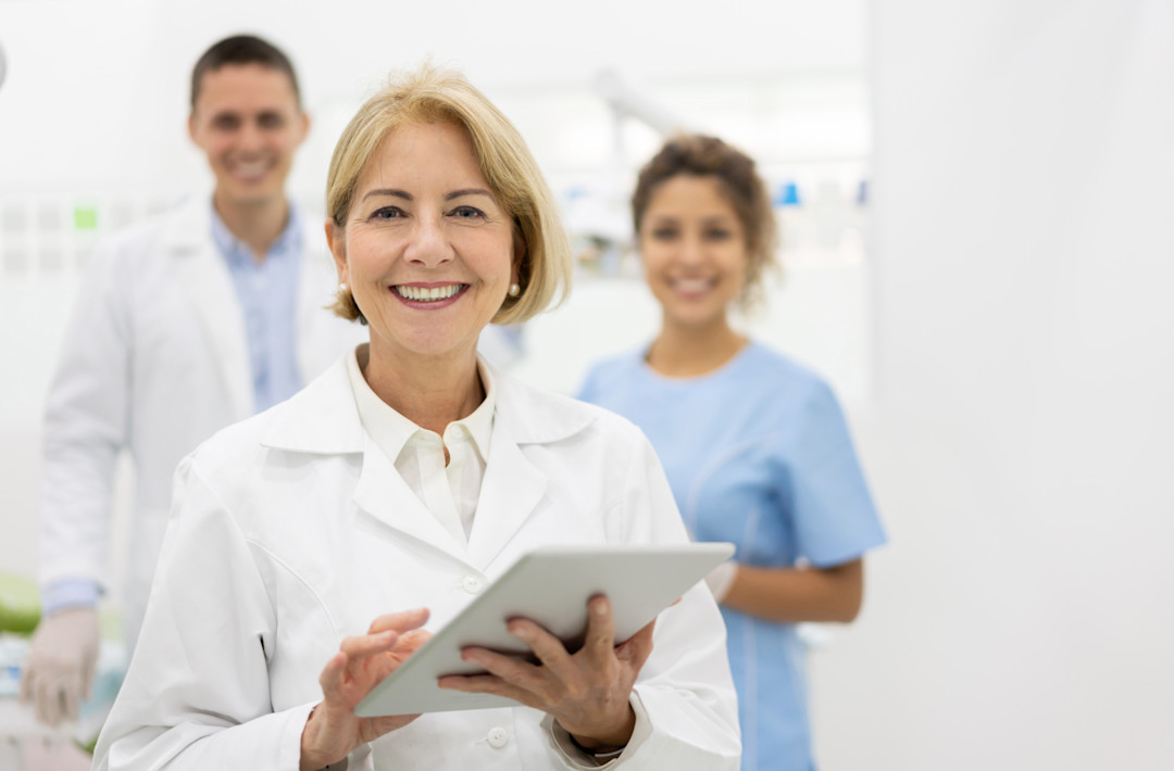 Smiling dermatologist with colleagues and a computer tablet