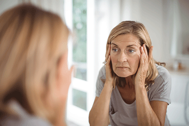 Senior woman looking in mirror pulling on sagging skin on her face