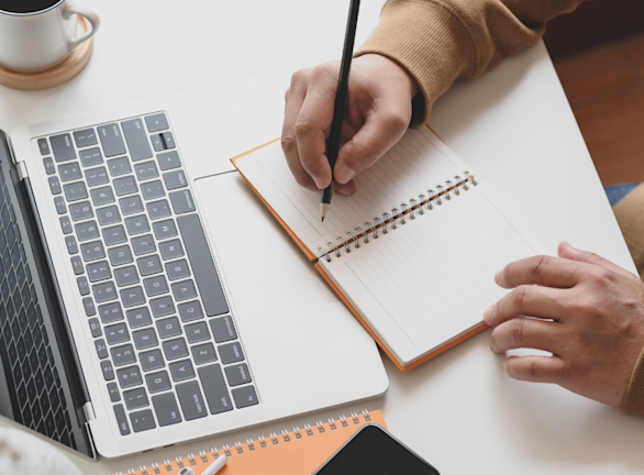 Man writing CV at desk with laptop and notepad
