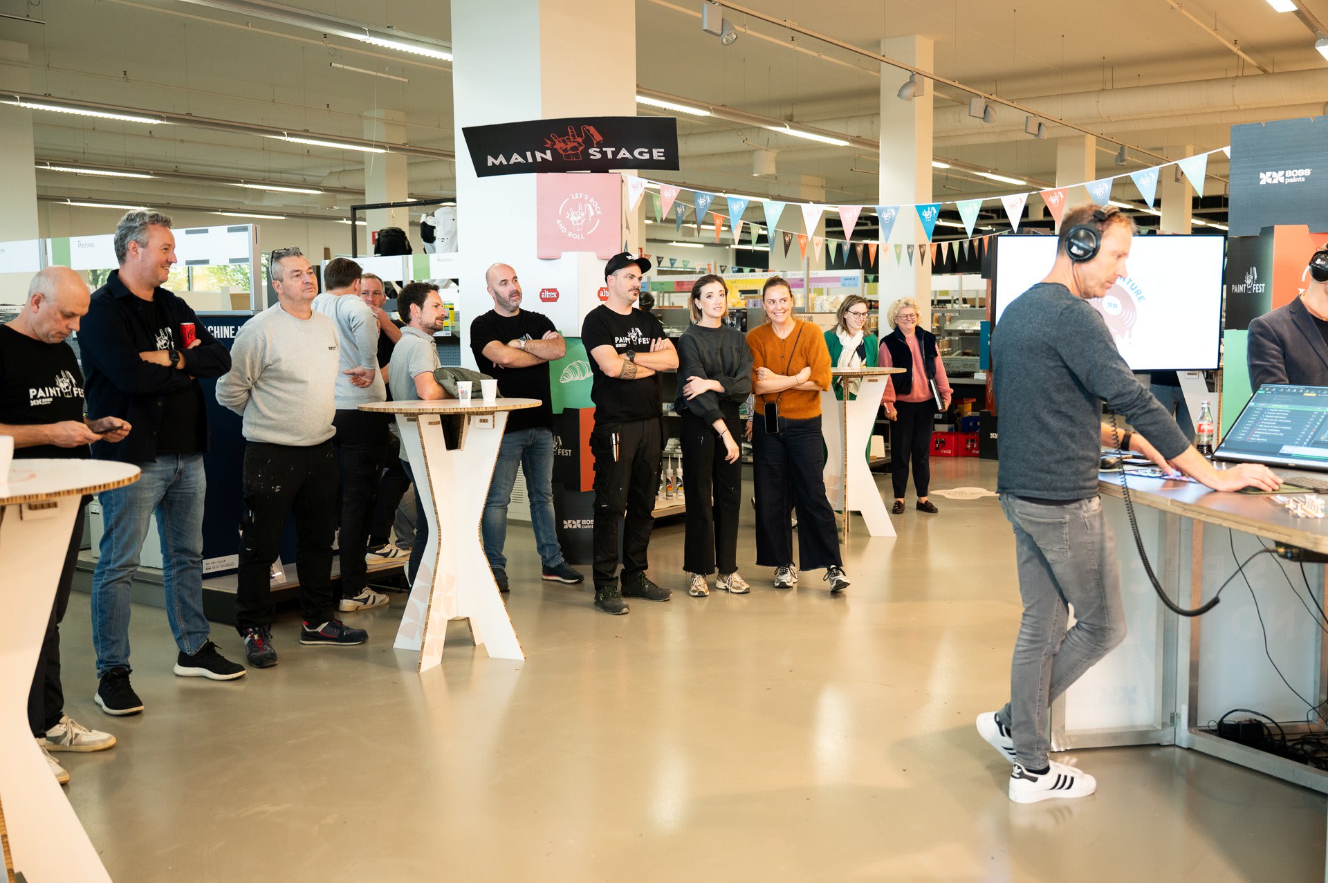 Een groep mensen staat te kijken naar een man die audioapparatuur bedient in een overdekte evenementenruimte met tafels en decoraties.