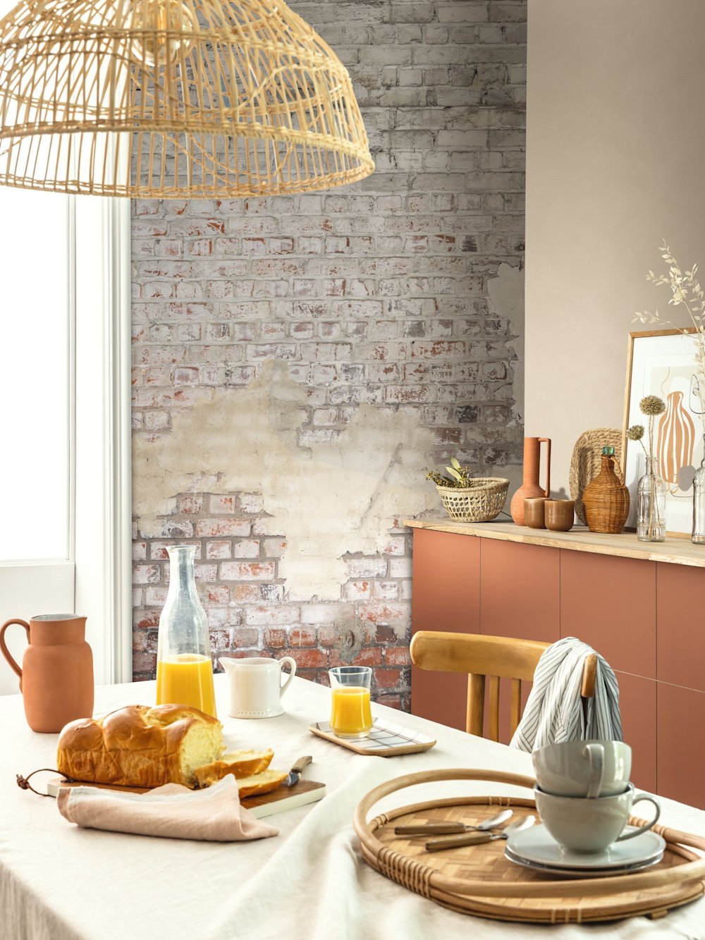 papier peint - salle à manger - Caselio - Kitchen box - KBO106251026 - blanc - rouge - Mur avec motif brique, armoires en terre cuite, table en bois, vaisselle et petit-déjeuner sur la table.