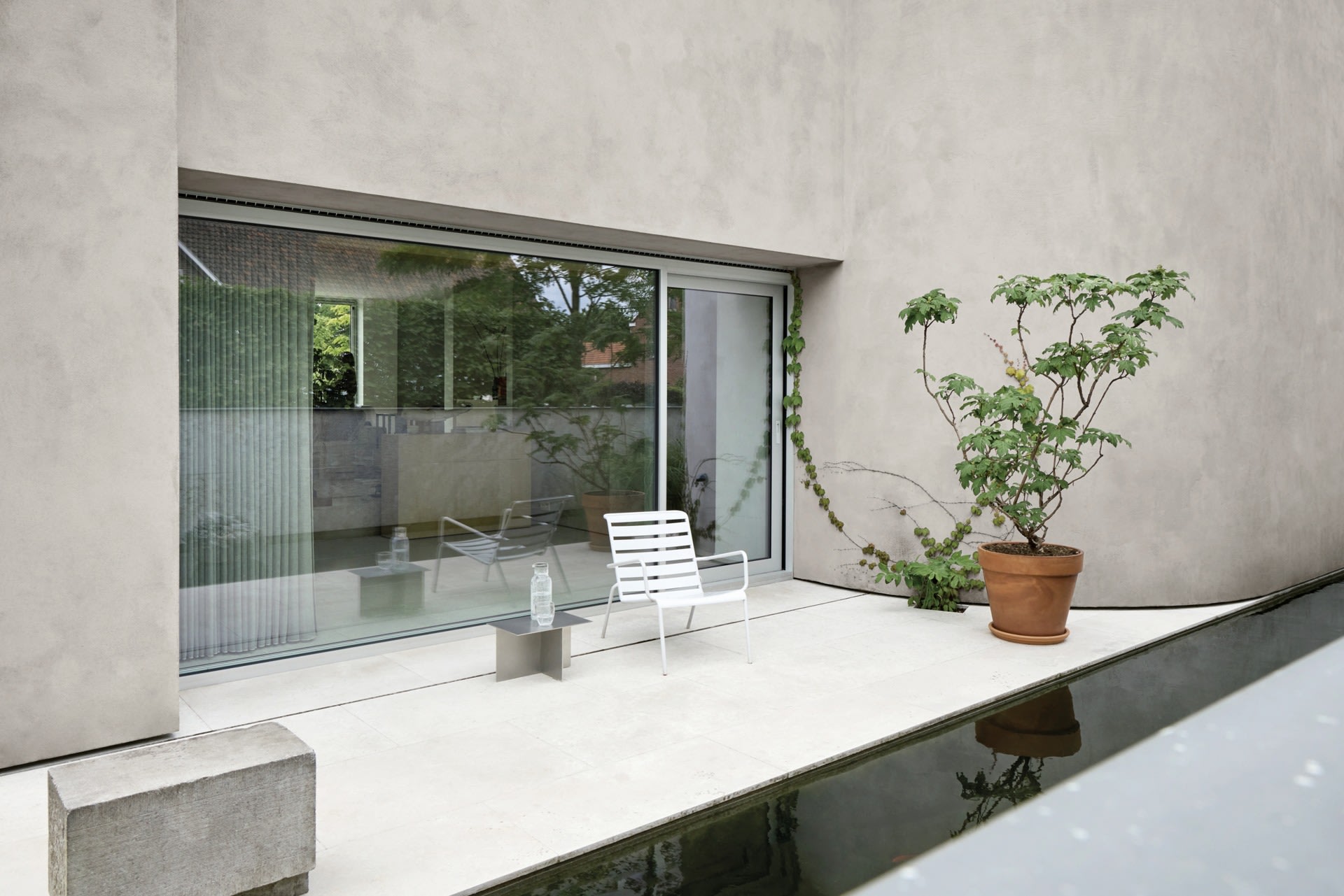Un mur moderne en béton aux angles vifs sépare un chemin pavé d'une végétation dense dans un jardin paysager.