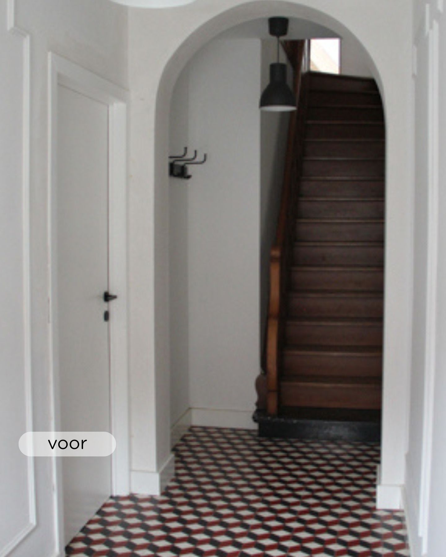 Een smalle gang met tegelvloer met patroon, witte muren, een gesloten witte deur aan de linkerkant, muurhaken en een donkere houten trap die naar boven leidt.
