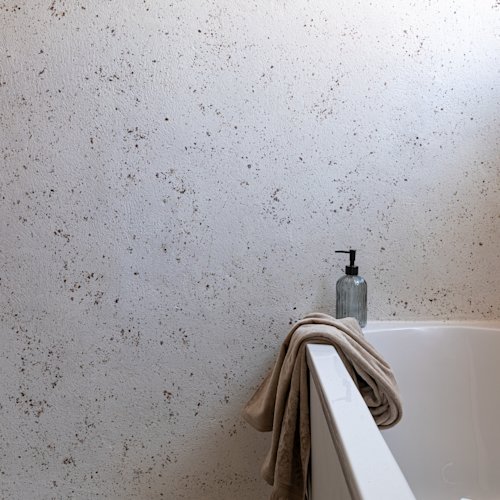 badkamer met terrazzo look op de muur, wit bad en zeepdispenser met bruine beige handdoek