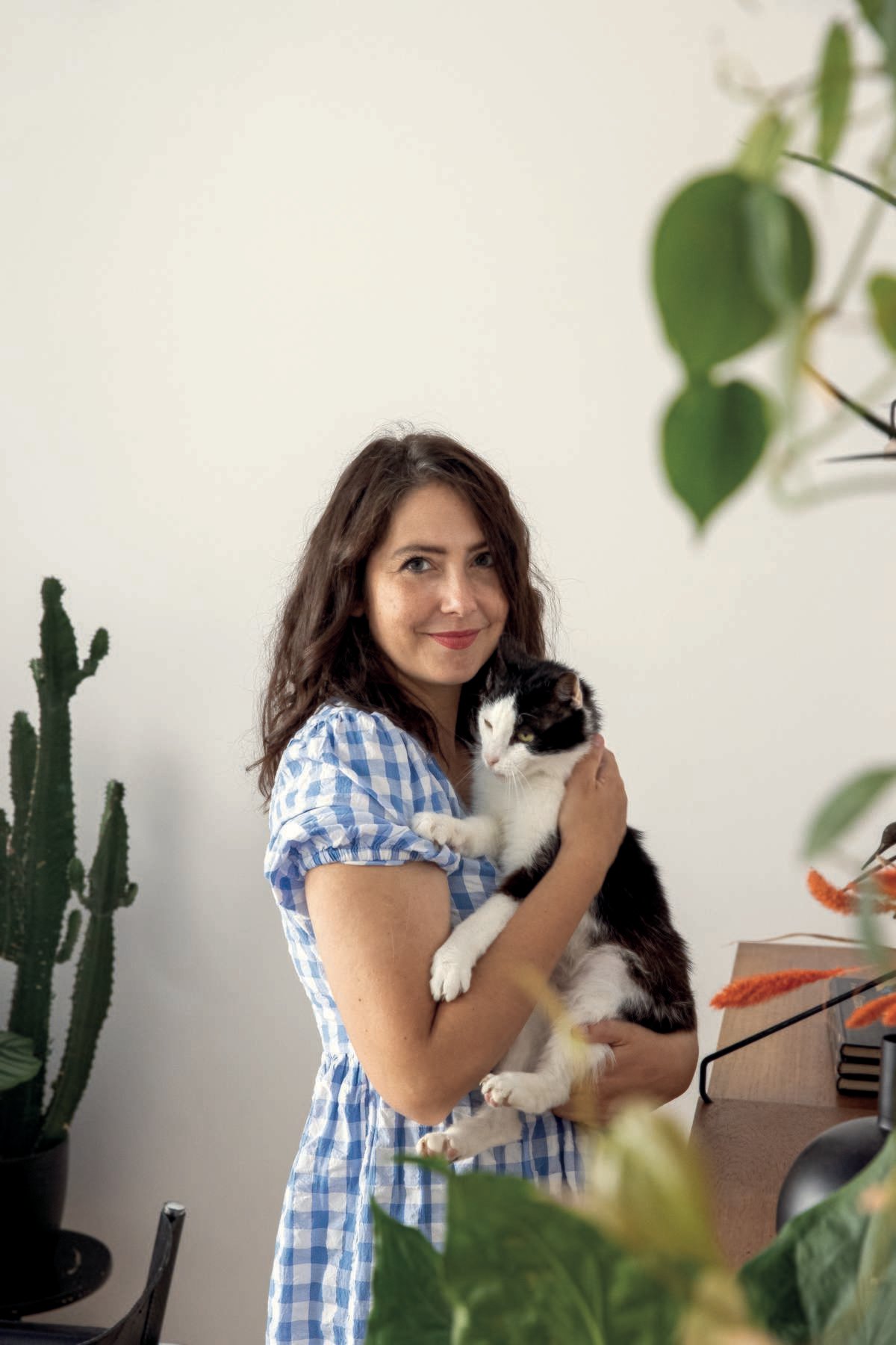 vrouw die kat vasthoudt aan een witte muur met planten op de achtergrond
