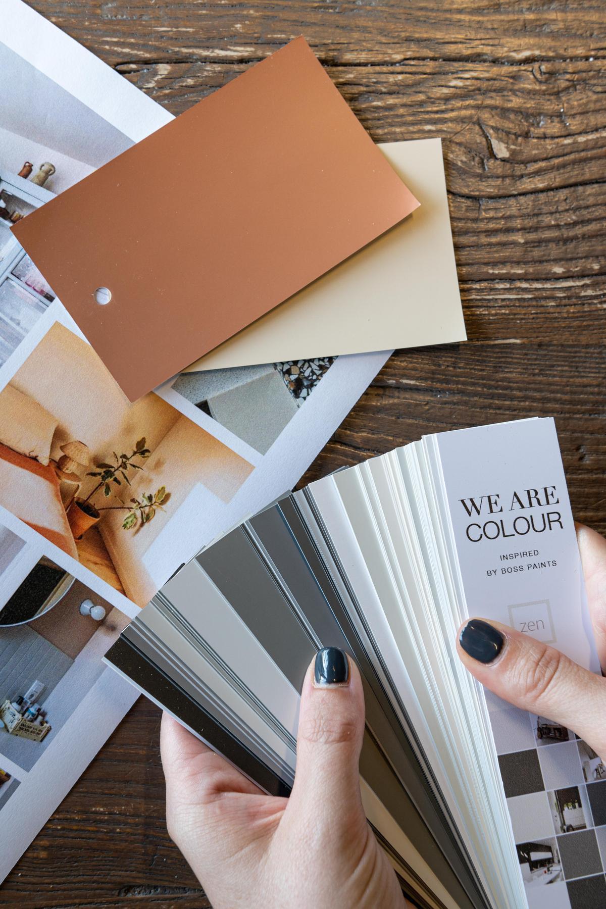 persoon die kleurwaaier vasthoudt in handen met moodboard en kleurkaartjes op de tafel