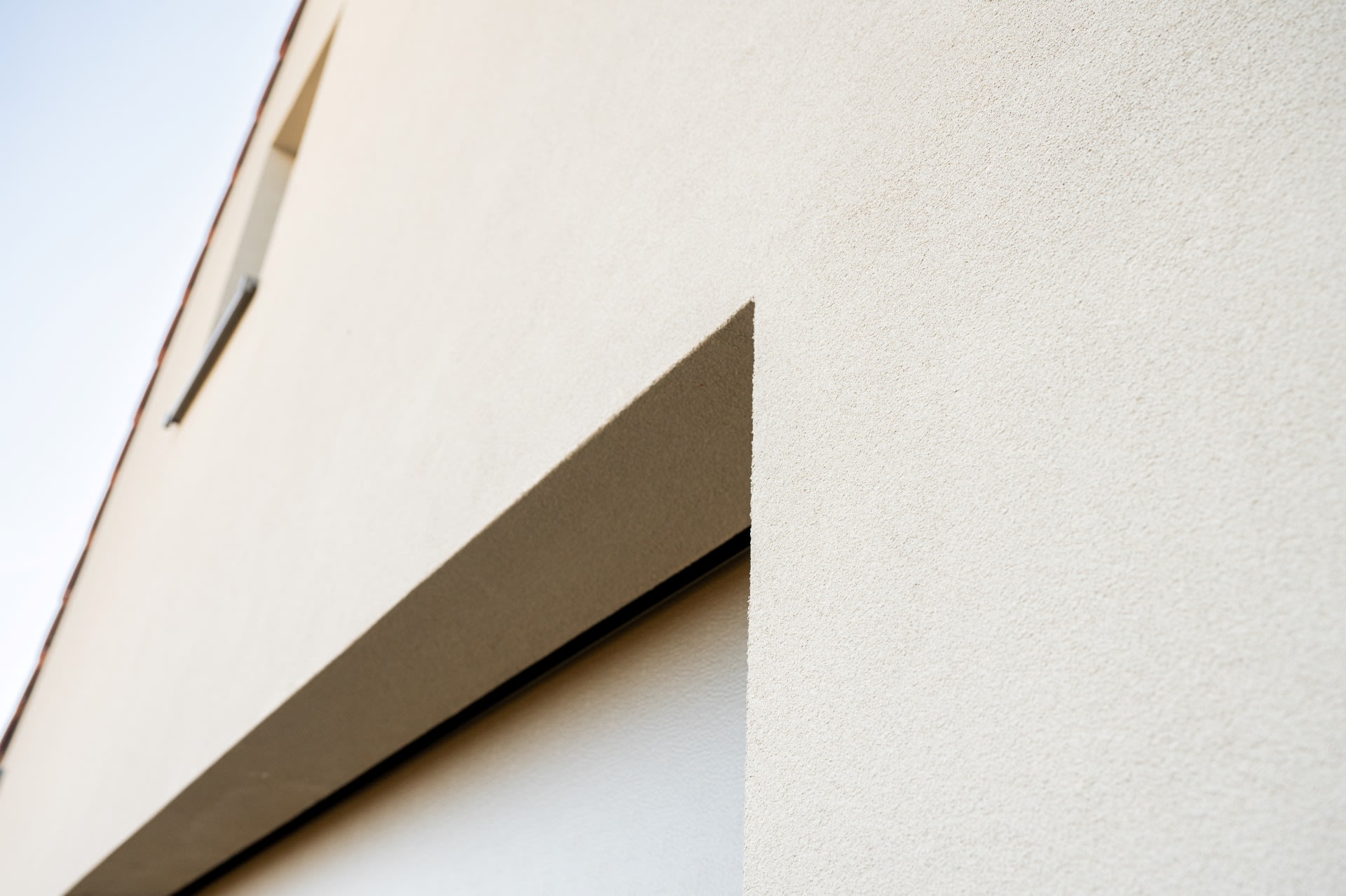 Gros plan d'une façade moderne, de couleur beige, aux lignes épurées et aux angles vifs, avec une petite fenêtre en haut