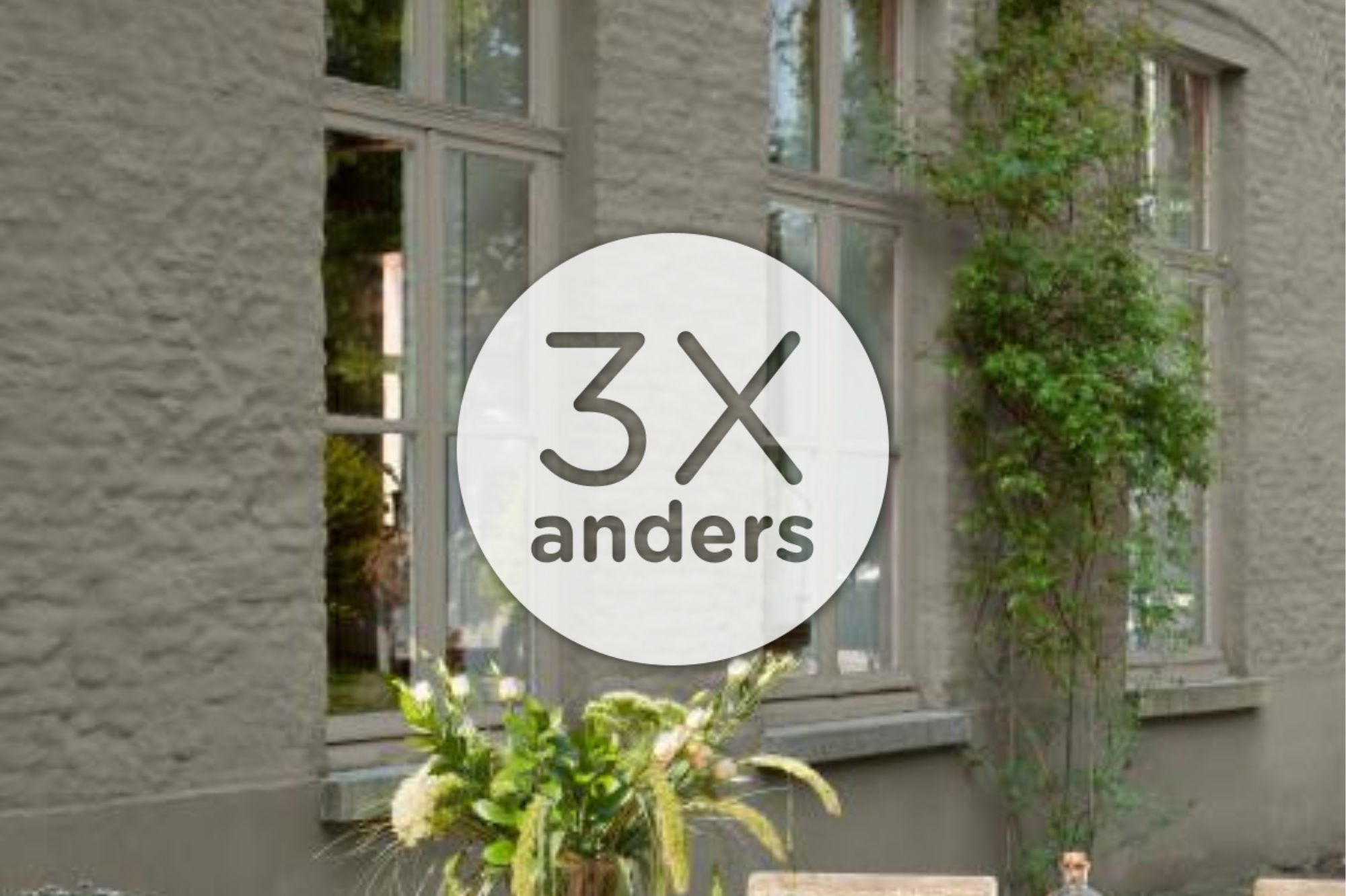 Een rond bord met "3X anders" in het midden is geplaatst boven een buitenaanzicht van een gebouw met grote ramen en een potplant.