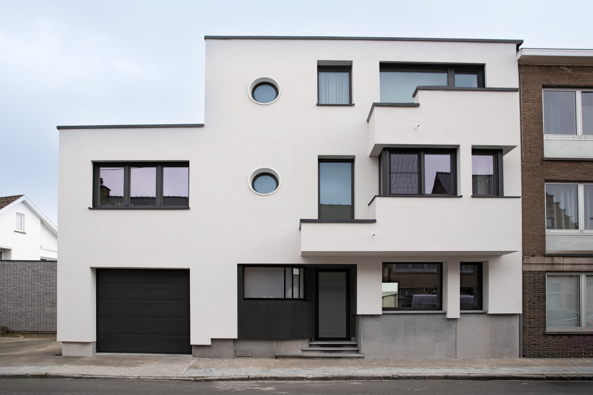 Une maison moderne en rangée de couleur blanche avec des lignes épurées, des fenêtres sombres et un garage à gauche