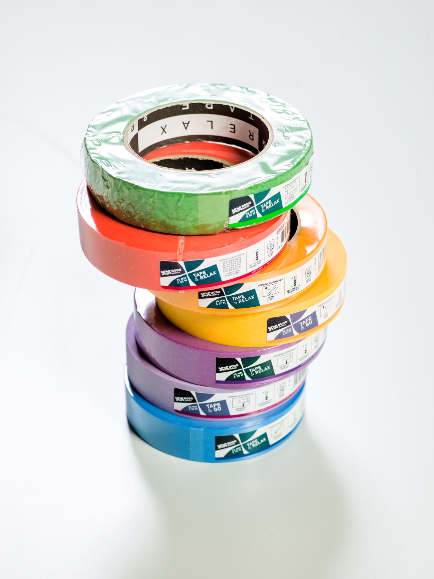Une pile de six rouleaux de ruban de masquage colorés - vert, rouge, orange, jaune, violet et bleu - disposés sur une surface blanche.