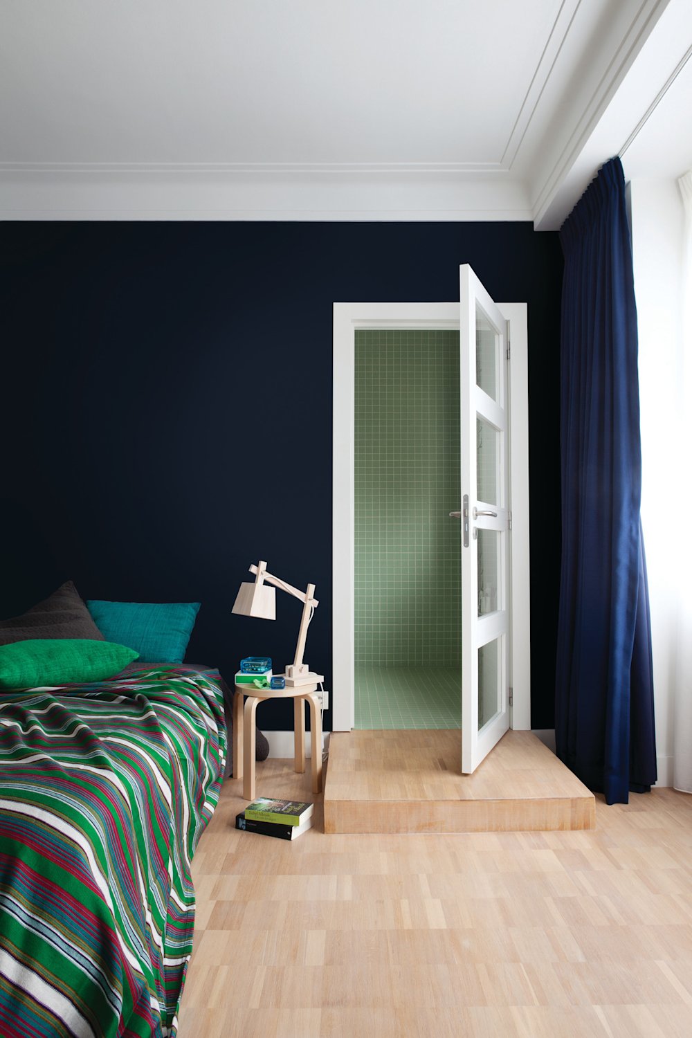 Colora-slaapkamer met donkerblauwe accentmuur achter het bed, wit plafond en witte deur