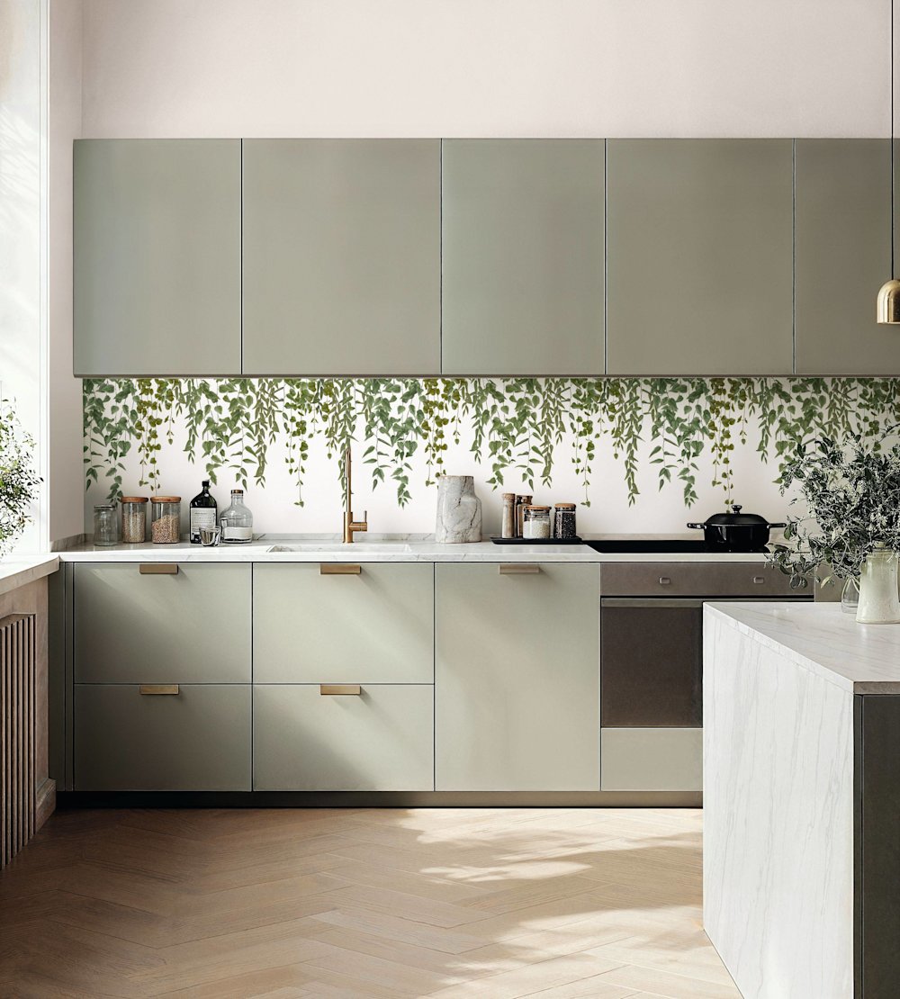 papier peint - cuisine - Caselio - Kitchen box - KBO106950723 - blanc - vert - Cuisine avec armoires gris-vert, papier peint à feuilles suspendues, sol en bois, îlot en marbre.