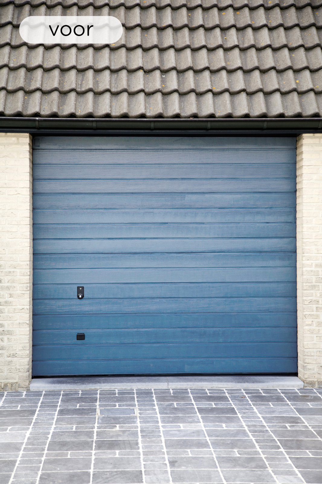 Gesloten blauwe garagedeur met horizontale panelen tussen lichtgekleurde bakstenen muren, onder een grijs pannendak en voor een stenen oprit.