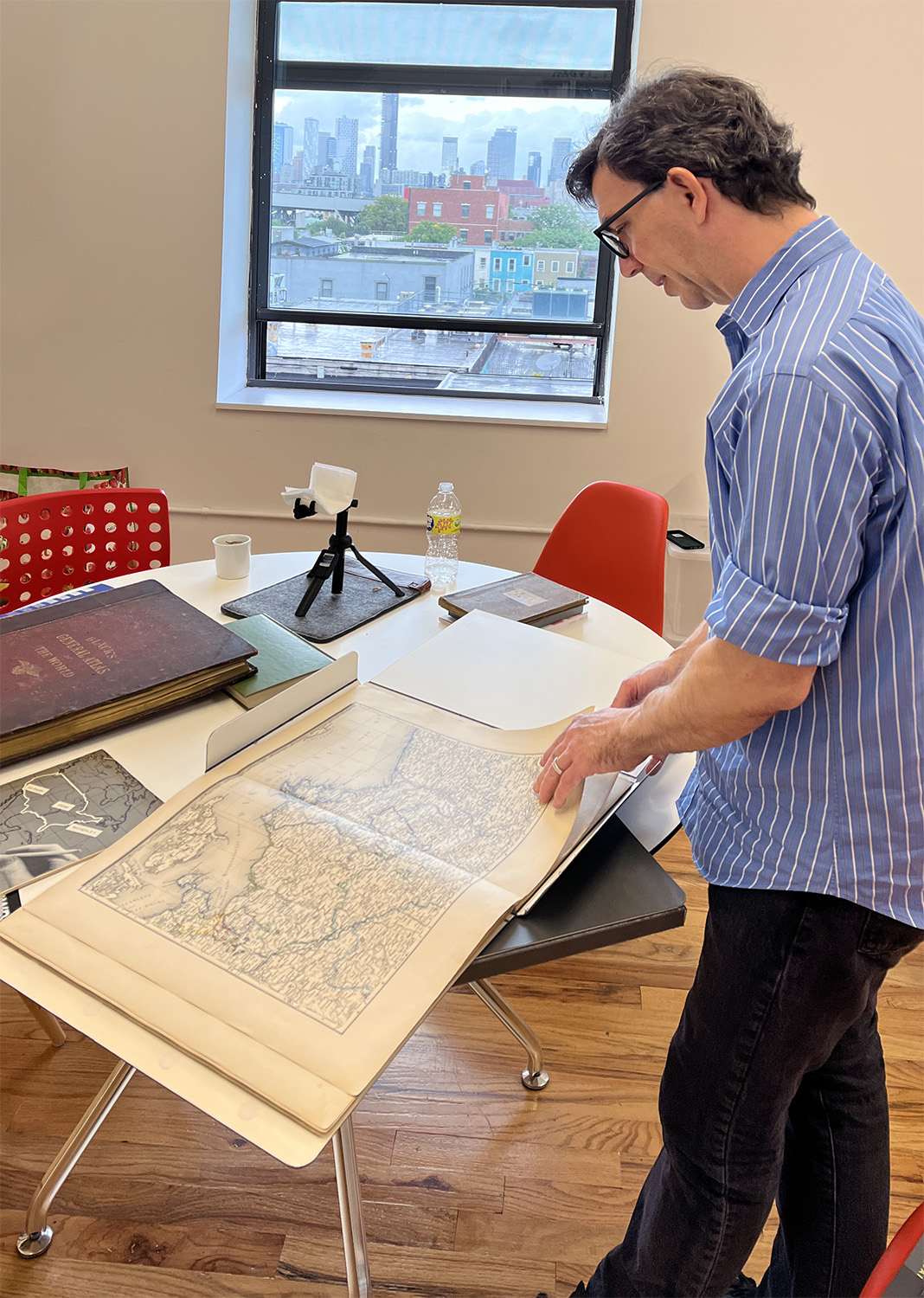 Tobias leafing through two of his collected atlases; [closed at left] Black’s General Atlas of the World, 1888[open] Marks’ World Atlas; circa 1890