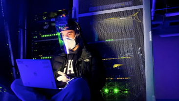 Man working inside data center, sitting on the floor with his computer.