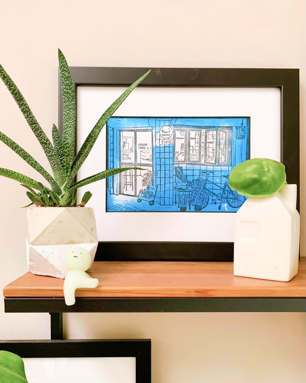 Framed artwork on a tabletop with small plants and a decorative object