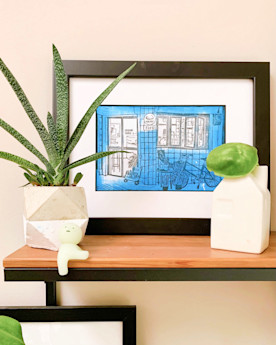 Framed artwork on a tabletop with small plants and a decorative object