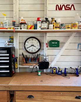 a wooden desk setup with an assortment of tools and finishes, a clock, a first aid kid, and a painted NASA logo