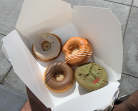 a photo of a hand holding a container holding three donuts and a muffin