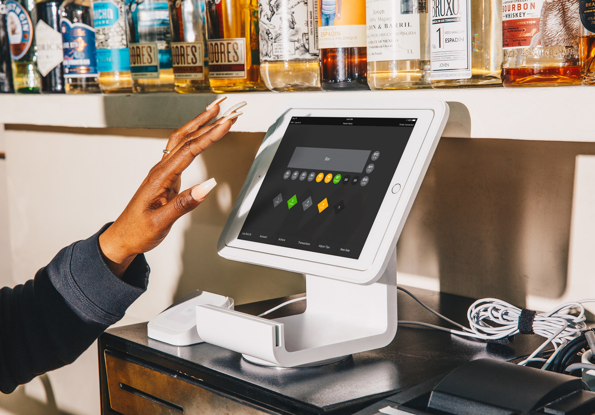 A woman's hand with manicured nails hovers over Square Stand with the restaurants screen featured.