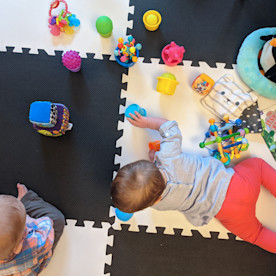 two toddlers playing with an assortment of toys on a black and white checkered puzzle mat
